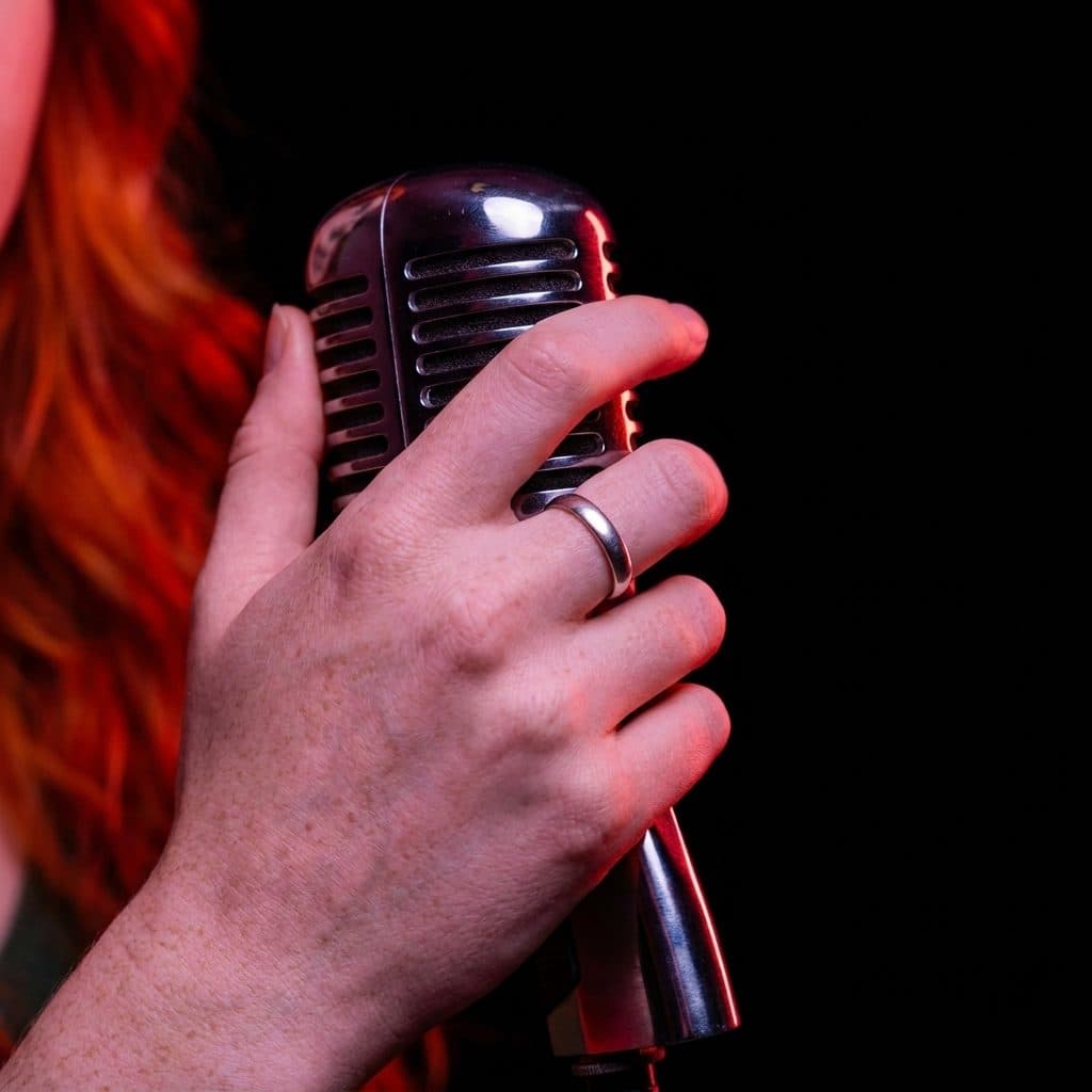 Close-up of Celeste’s ringed hand resting on a vintage microphone.